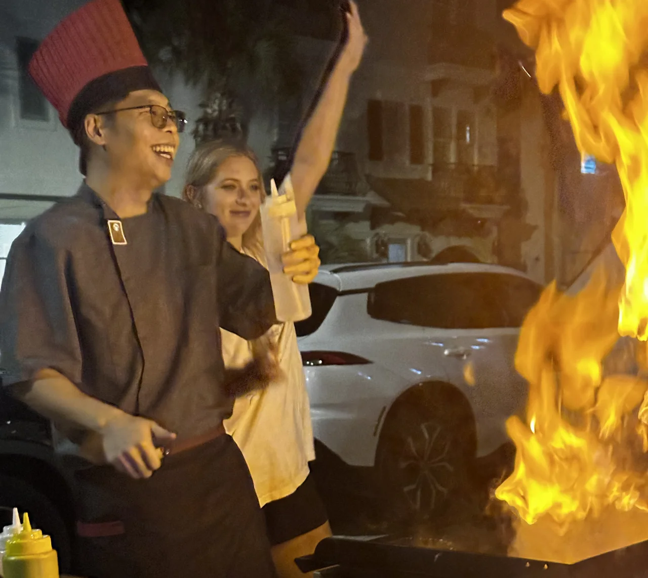 Hibachi chef and guest smiling beside a large flame during a private party